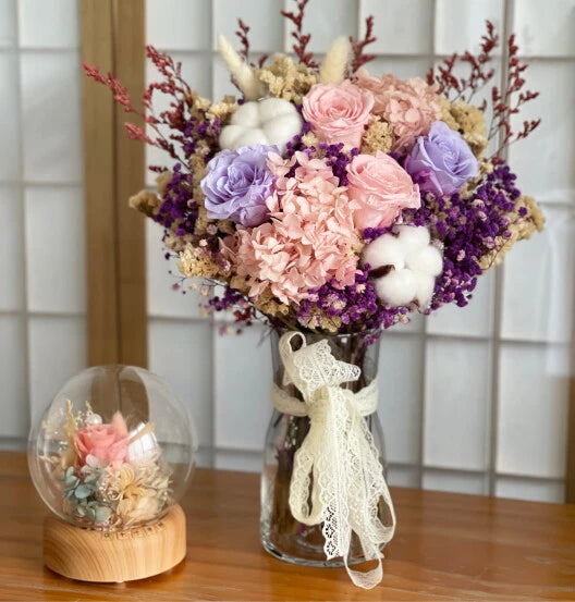 En vase med rosa, lilla og brune blomster.