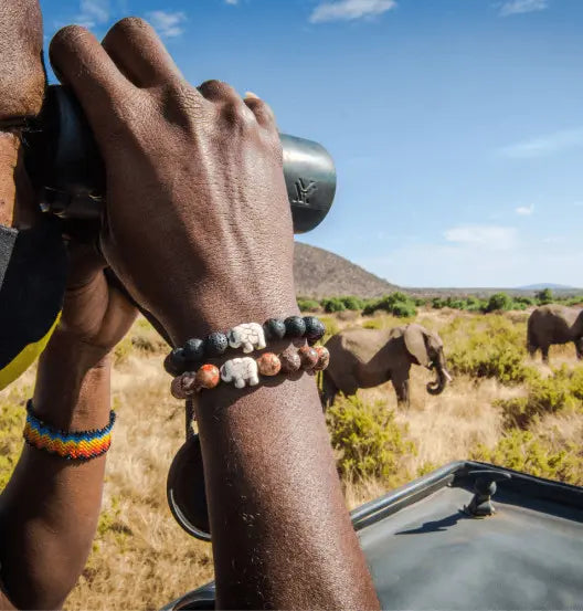 Una persona che indossa un braccialetto Fahlo mentre osserva degli elefanti da un binocolo.