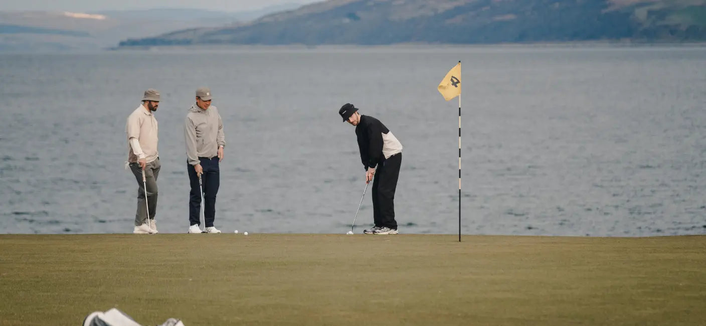 Three men on a putting green beside the water