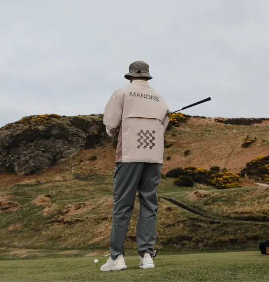 Man wearing a Manors jacket setting up a golf tee