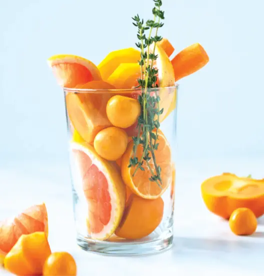 Glass filled with orange fruits and vegetables.