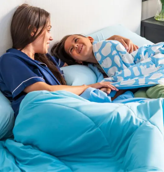 Mother and daughter laying in bed with blue sheets.