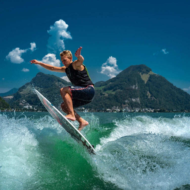 Person surfing on a wake with a mountainous background.