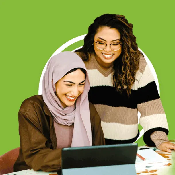 Duas mulheres sorrindo e trabalhando em um laptop.