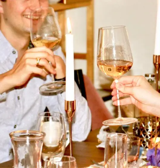 Two people cheers-ing wine glasses at a dinner table