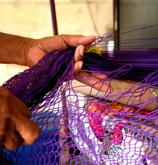 Manos de un hábil artesano tejiendo uno de los productos de Hamuhk con un hilo morado brillante
