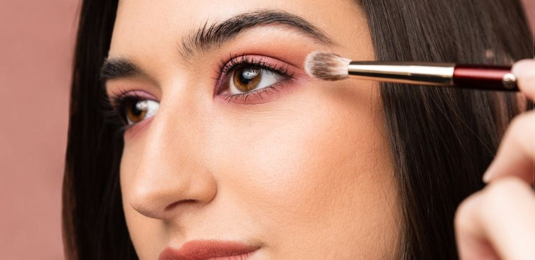 Close-up van een vrouw die roze oogschaduw op haar ooglid aanbrengt met een kwast